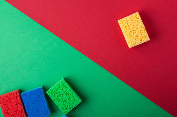 Green, red, blue, yellow sponges on green and red colored paper background, copy space, top view, flat lay - Photo, Image