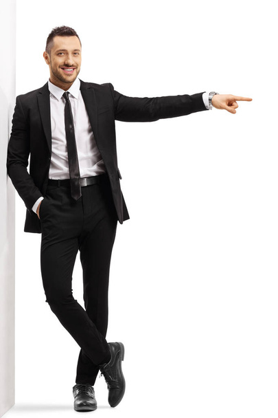 Businessman leaning on a wall and pointing to the side - Fotoğraf, Görsel