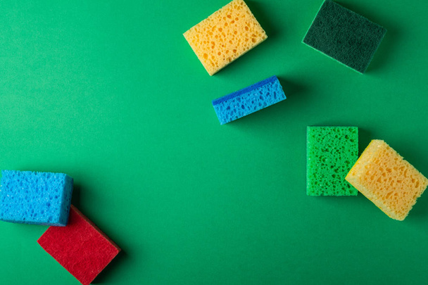 Scattered yellow, green, red, blue sponges on green colored paper background, copy space, top view, flat lay - Foto, Imagem