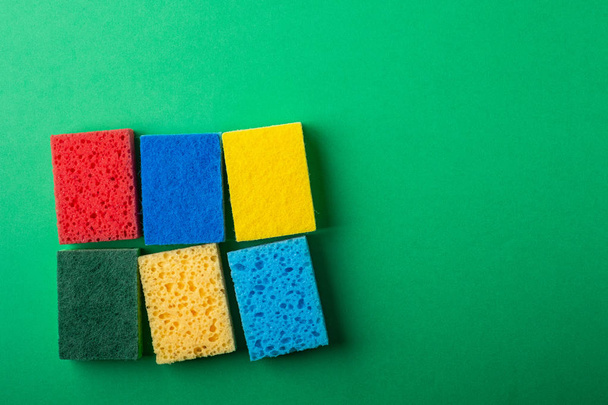 Yellow, green, red, blue sponges on green colored paper background, copy space, top view, flat lay - 写真・画像