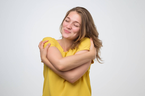 Positive relaxed young woman closing eyes with pleasure, keeping arms around herself - Photo, image
