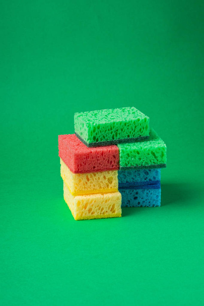 Stack of sponges in red, blue, green, yellow colors on green paper background, close up - Фото, зображення