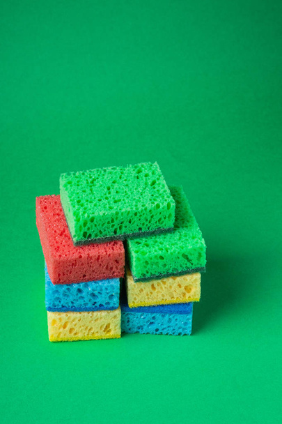 Stack of sponges in red, blue, green, yellow colors on green paper background, close up - Foto, Imagen