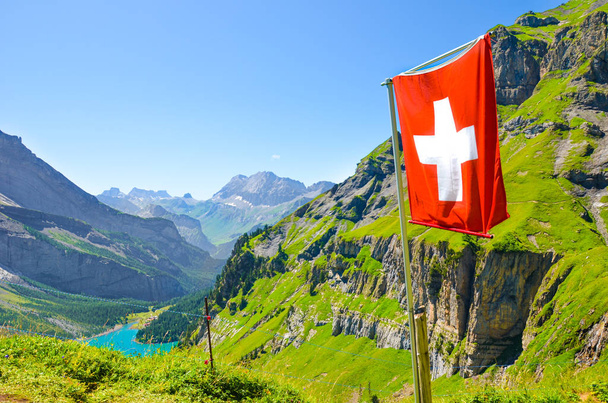 Integetett zászlaja Svájc a hegyen a svájci Alpokban. Türkiz Oeschinensee a háttérben. Nemzeti koncepció. Svájc nyár. Alpesi táj. Csodálatos természet. Turistalátványosságok - Fotó, kép