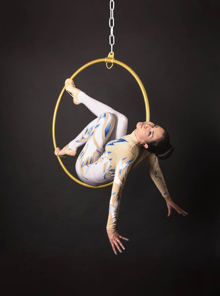 A slender,dark-haired girl - an air acrobat in a white and blue suit, performs exercises in an air ring. - Foto, afbeelding