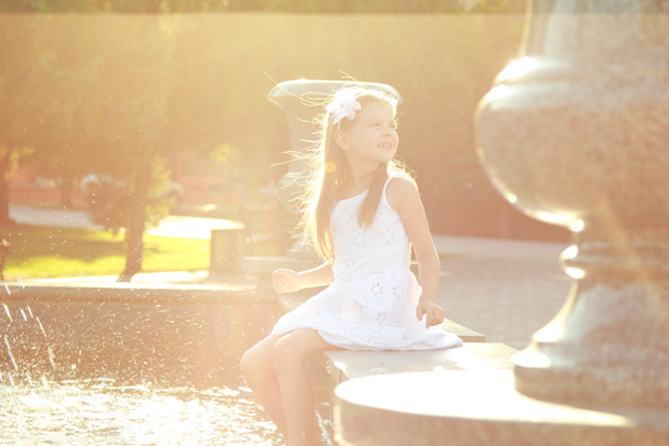 Encantadora niña alegre en un vestido blanco y disfrutando de las salpicaduras de agua fría en la fuente
 - Foto, imagen