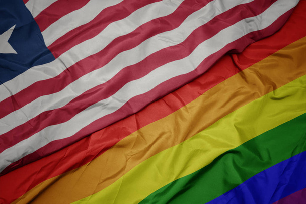 waving colorful gay rainbow flag and national flag of liberia. - Photo, Image