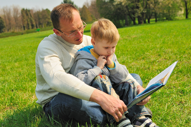 kisfiú és apja olvasó egy könyv szabadtéri - Fotó, kép