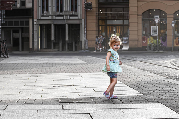 Little cute blonde girl child standing in the town square. - Zdjęcie, obraz