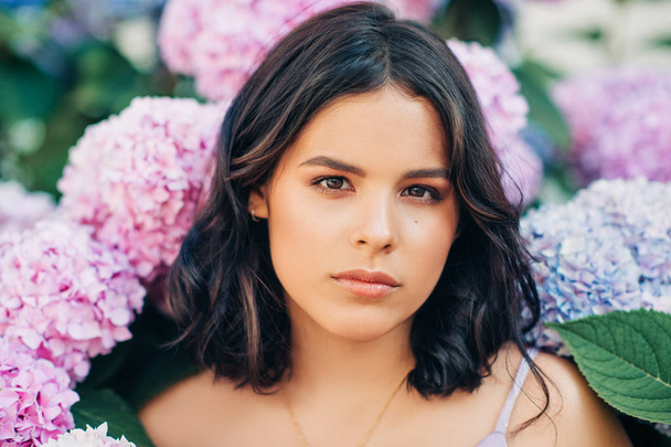 Outdoor portrait of beautiful young woman posing in pink hydrangea flowers - Foto, Imagem