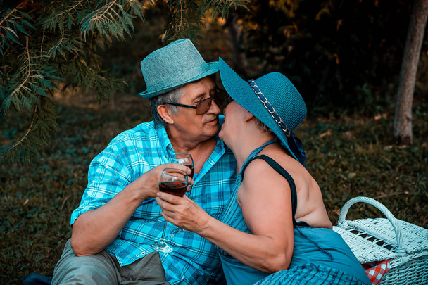 Vanhempi pari suutelee juodessaan viiniä piknikillä
 - Valokuva, kuva