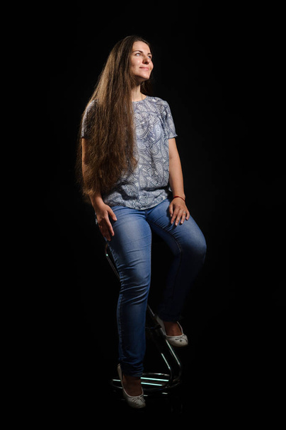 woman sitting in a chair. Studio picture, black background - Foto, afbeelding