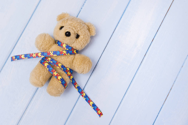 Wereld Autisme Awareness Day, geestelijke gezondheidszorg concept met teddybeer en lint puzzel patroon. Op blauwe backgroun - Foto, afbeelding
