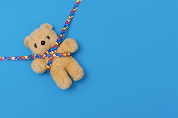 Wereld Autisme Awareness Day, geestelijke gezondheidszorg concept met teddybeer en lint puzzel patroon. Op blauwe backgroun - Foto, afbeelding