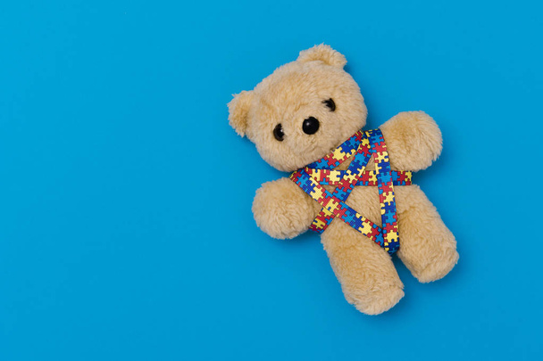 Día Mundial del Autismo, concepto de cuidado de la salud mental con oso de peluche y patrón de rompecabezas de cinta. Sobre fondo azul
 - Foto, Imagen