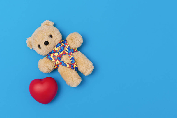 Всемирный день осведомленности об аутизме, концепция психиатрической помощи. Медведь Тедди с красным сердцем и рисунком головоломки ленты. На синем фоне
 - Фото, изображение