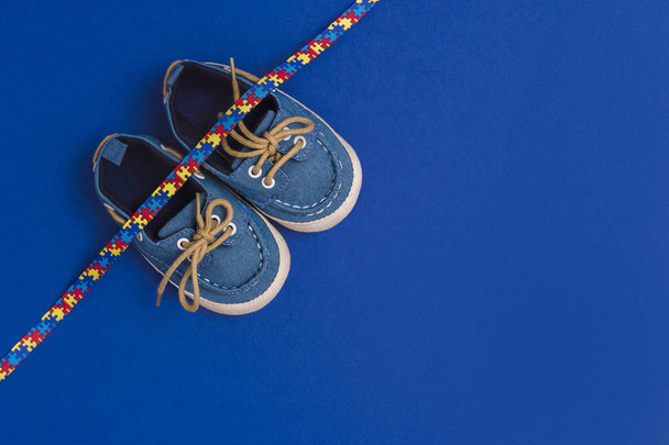 Światowy dzień świadomości autyzmu, koncepcja opieki zdrowotnej z niebieskimi butami dla niemowląt i wzorem układanki wstążki. Na niebieskim oświetlenie tła - Zdjęcie, obraz