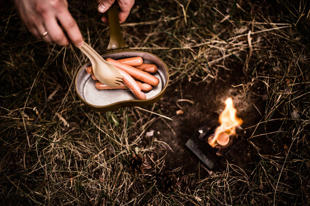 As linguiças fritam-se sobre uma fogueira aberta em uma panela
 - Foto, Imagem