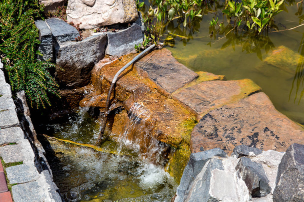 Kamienny wodospad kaskadowy w sztucznym stawie z wodą w parku w słoneczny dzień. - Zdjęcie, obraz