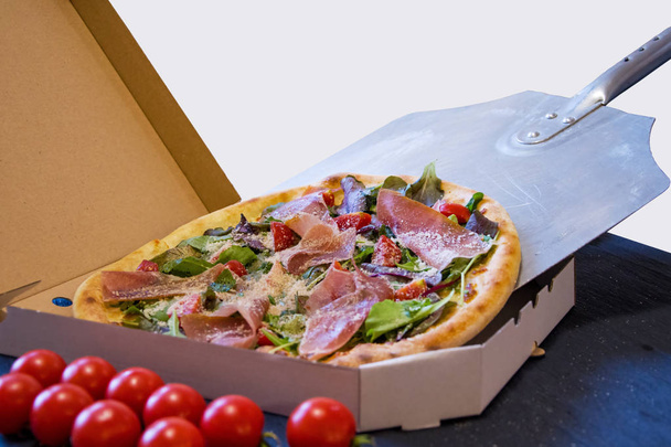 Pizza caliente cocida en una pala se empuja en una caja de embalaje, entrega de alimentos
 - Foto, imagen