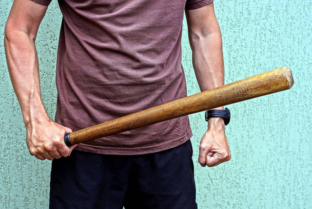wooden bat in a mans hand against a gray wall - Foto, afbeelding