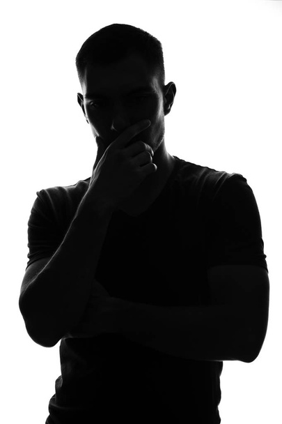Silhouet portret van een doordachte jonge man die zijn hand vasthoudt aan zijn gezicht, de pose van een denker - Foto, afbeelding