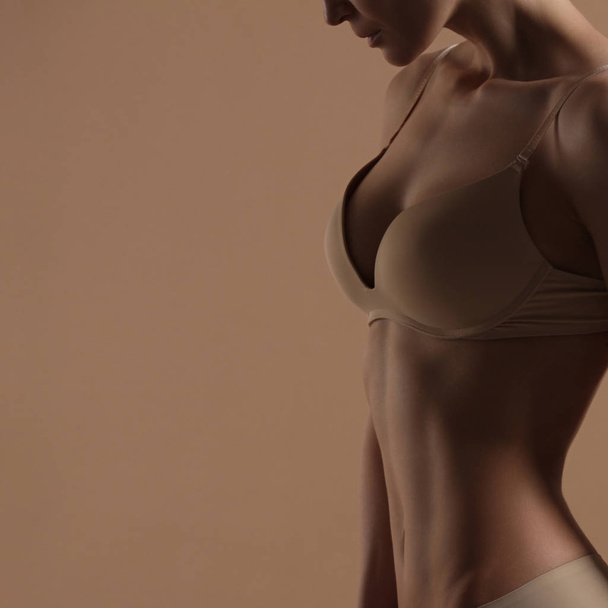 Thin young woman in underwear on beige background - 写真・画像