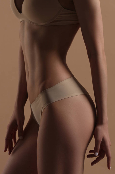 Thin young woman in underwear on beige background - Фото, зображення