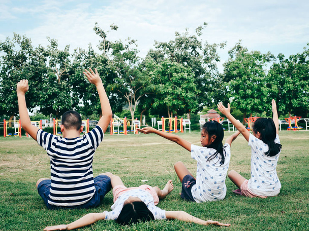 Задняя часть мальчика и девочки, сидящих на зеленой траве в парке на открытом воздухе
. - Фото, изображение
