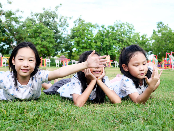 Happy Asian girls laying down on green grass outdoor together, l - Photo, Image