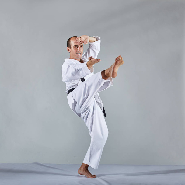 In karategi, an athlete performs formal karate exercises on a gray background - Fotoğraf, Görsel