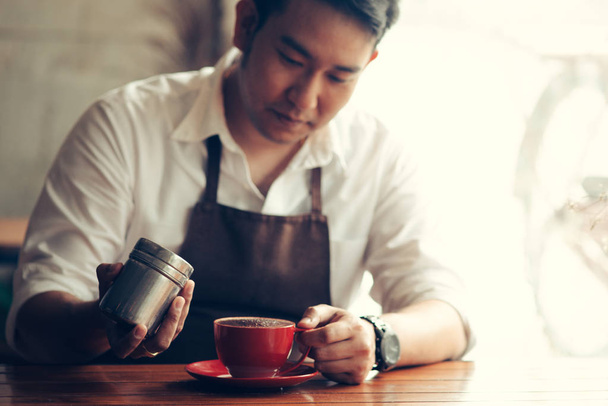 Asian barista sprinkles chocolate powder on drink in red cup. - Фото, зображення