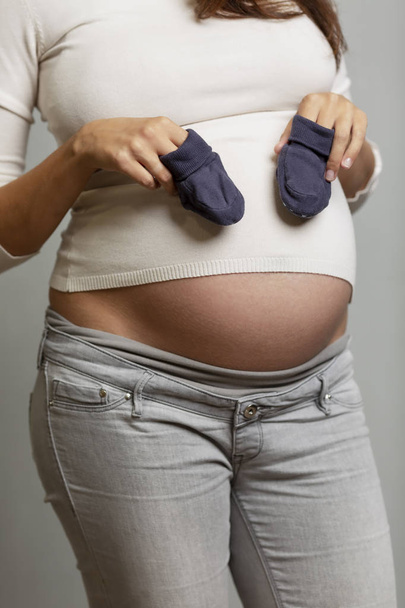 A pregnant woman with a big belly with baby booties in her hands.  - Foto, immagini