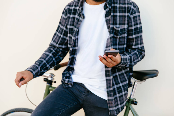 Vista de cerca del hombre sosteniendo un teléfono inteligente, mientras está sentado en bicicleta, al aire libre
. - Foto, Imagen