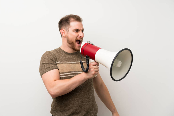 Handsome man over isolated white wall shouting through a megaphone - Photo, Image