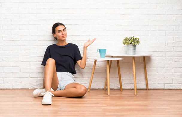 Молодая женщина, сидящая на полу с воображаемым копирайтом на ладони
 - Фото, изображение