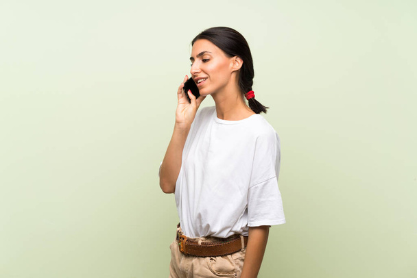Молодая женщина на изолированном зеленом фоне с помощью мобильного телефона
 - Фото, изображение