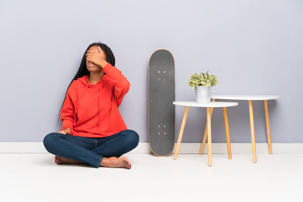 African American skater teenager girl with braided hair sitting on the floor covering eyes by hands - Foto, imagen