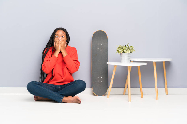 驚きの表情で床に座って編組髪を持つアフリカ系アメリカ人のスケーターティーンエイジャーの女の子 - 写真・画像