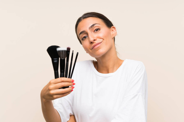 Mujer joven sosteniendo una gran cantidad de cepillo de maquillaje haciendo gesto dudas mientras levanta los hombros
 - Foto, Imagen