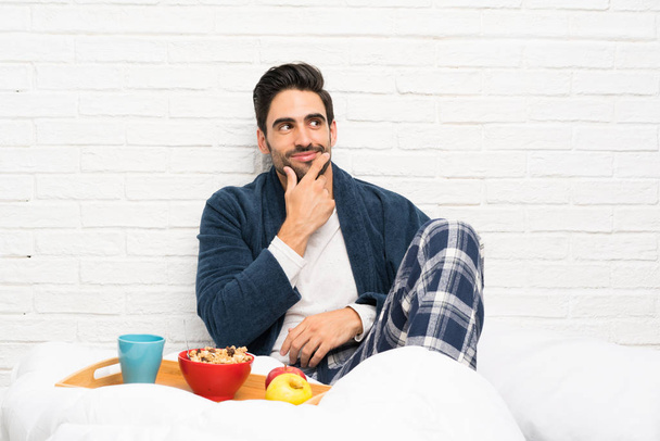 Uomo a letto con vestaglia e fare colazione pensando a un'idea
 - Foto, immagini