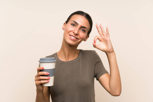 Młoda kobieta trzyma kawę zabrać pokazując OK znak z palcami - Zdjęcie, obraz