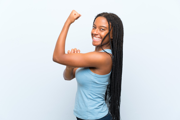 afrikanisch-amerikanische Teenager-Mädchen mit langen geflochtenen Haaren über isolierten blauen Hintergrund macht starke Geste - Foto, Bild