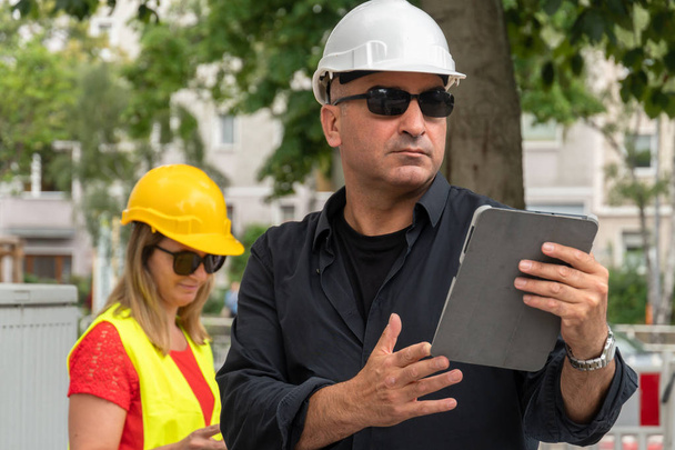 Ingenieros absorbidos con cascos de protección en el trabajo con documentos y una tableta en el sitio de construcción
 - Foto, Imagen