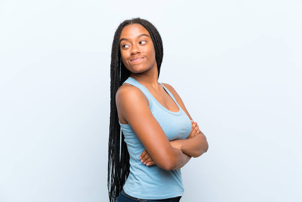 孤立した青い背景の上に長い編組髪を持つアフリカ系アメリカ人のティーンエイジャーの女の子笑い - 写真・画像