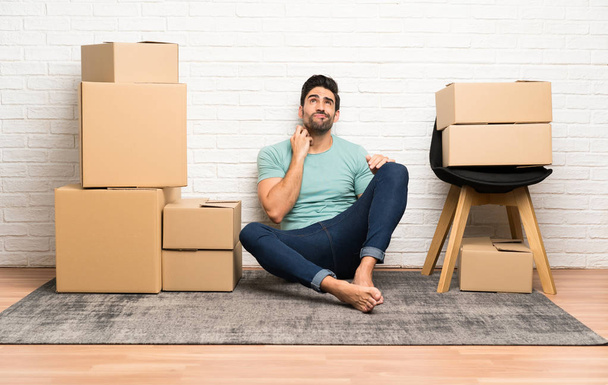 Handsome young man moving in new home among boxes thinking an idea - Photo, Image