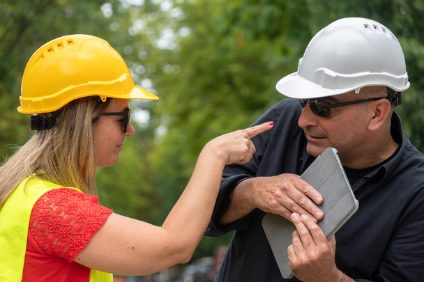 Angry chefe da construção gritando e apontando o dedo para um arquiteto penitente que se defende com um computador tablet digital
 - Foto, Imagem