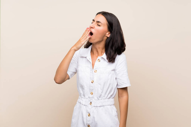 Молодая женщина на изолированном фоне зевает и закрывает широко раскрытый рот рукой - Фото, изображение