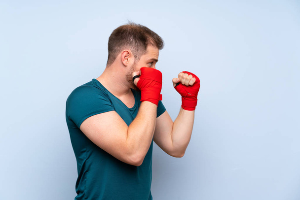 Blonde sport man over blue wall in boxing bandages - Foto, Bild
