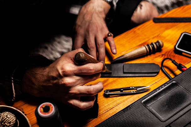 Man makes a leather product, and polishes it in a home workshop. On a wooden table. - Photo, Image